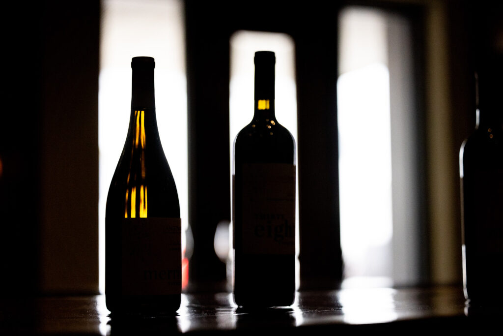 Wine bottles backlit by windows within darkly lit room